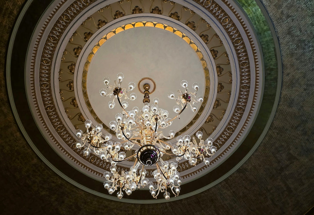 A grand ornate chandelier hangs from a decorative ceiling