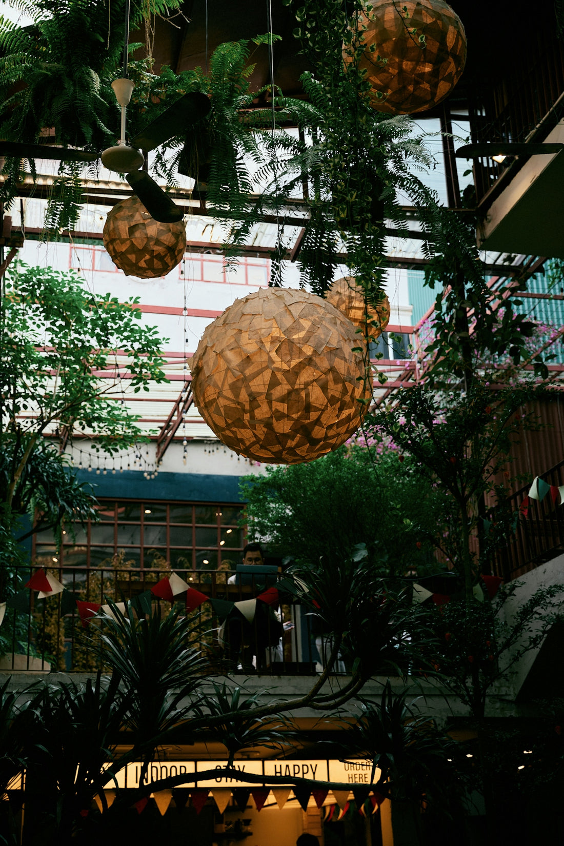 Hanging spherical lanterns amidst lush indoor plants.