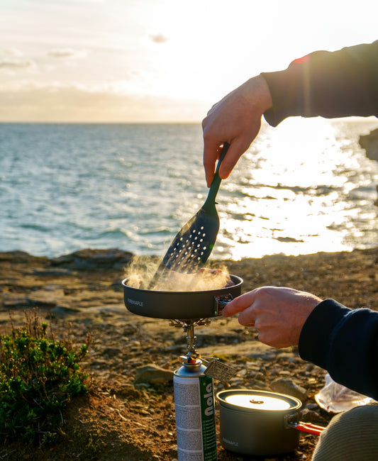 Person cooking outdoors by the ocean at sunset