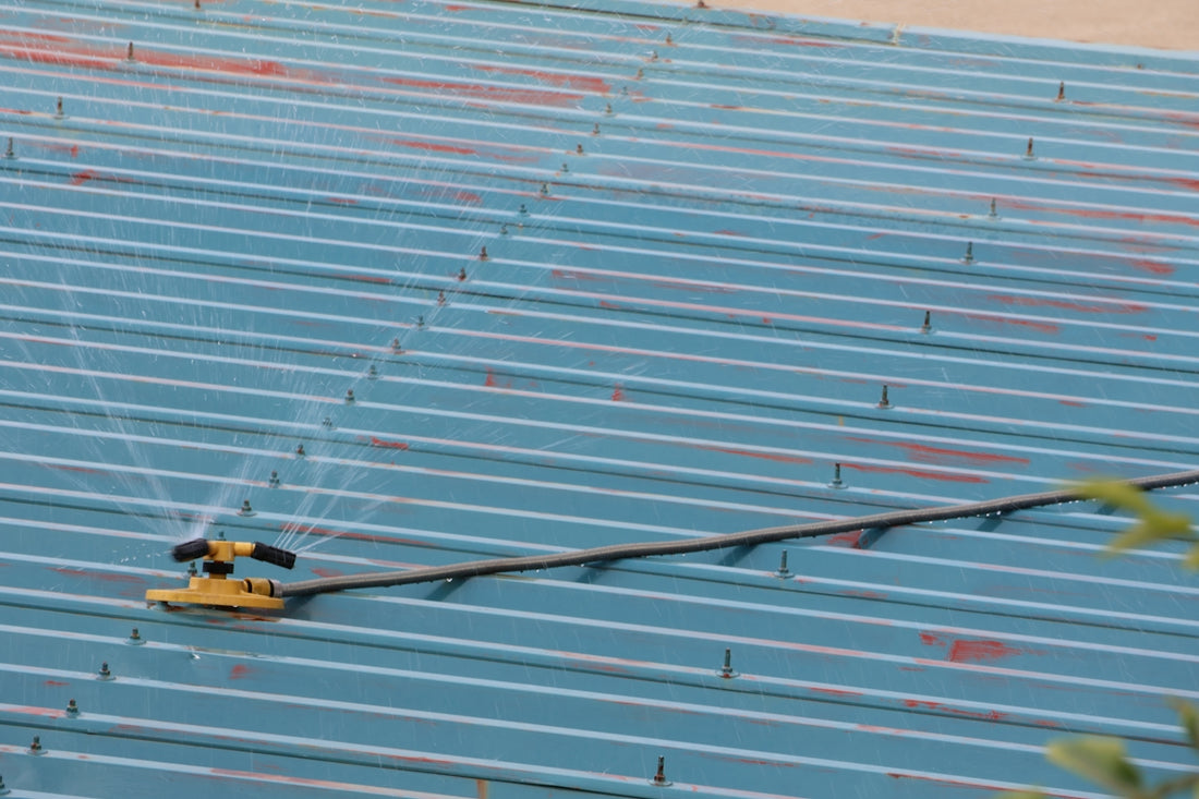 A yellow sprinkler system waters a blue corrugated roof.