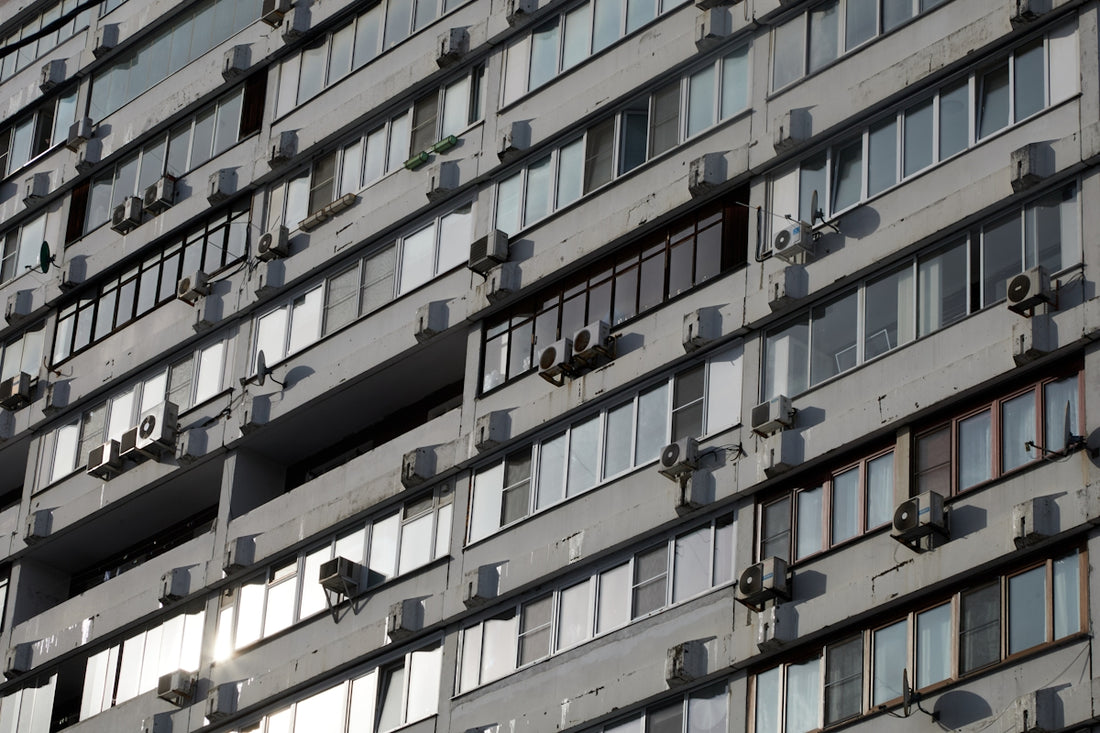 A concrete building facade with many windows and air conditioners