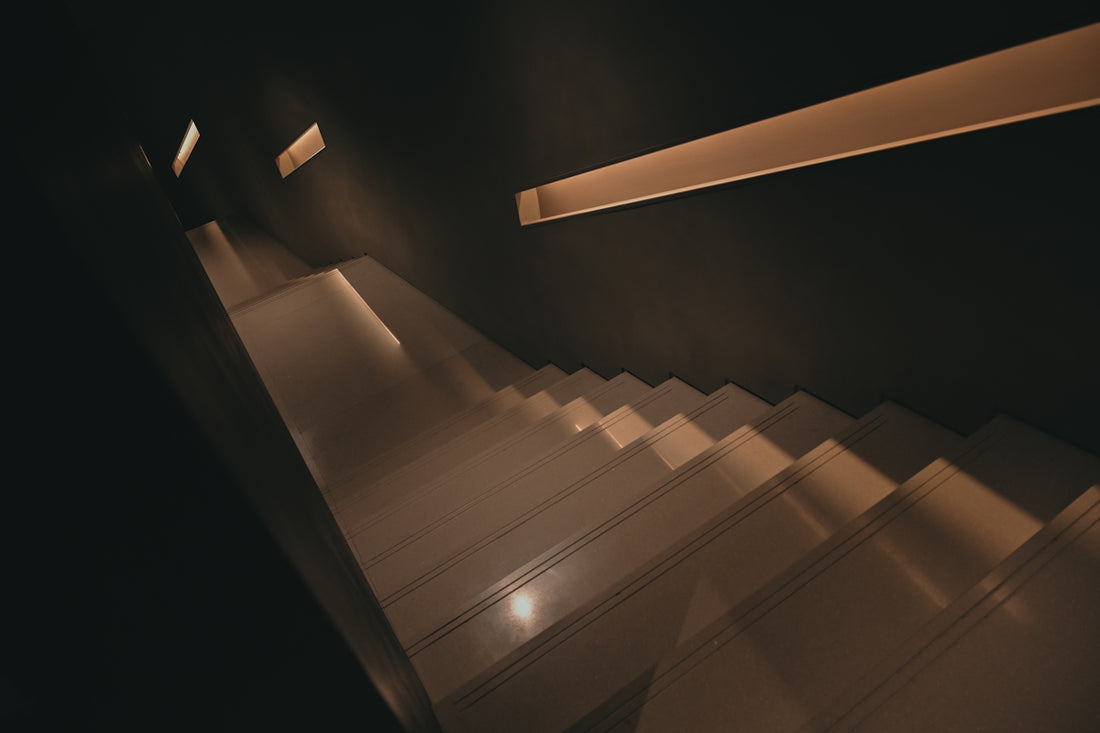 Dark, minimalist staircase illuminated by warm strip lighting
