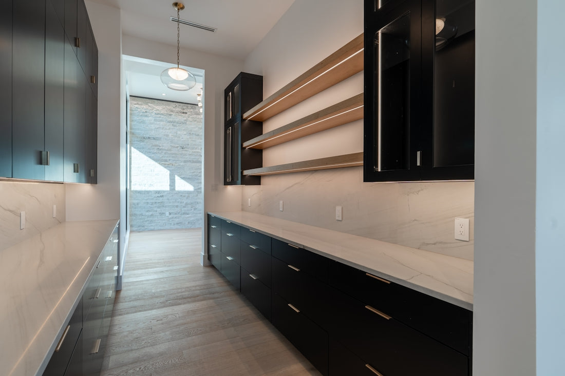 Modern pantry with dark cabinets, light countertops, and wooden shelves.