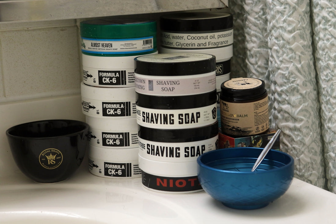 Various shaving soaps and bowls on a bathroom counter.