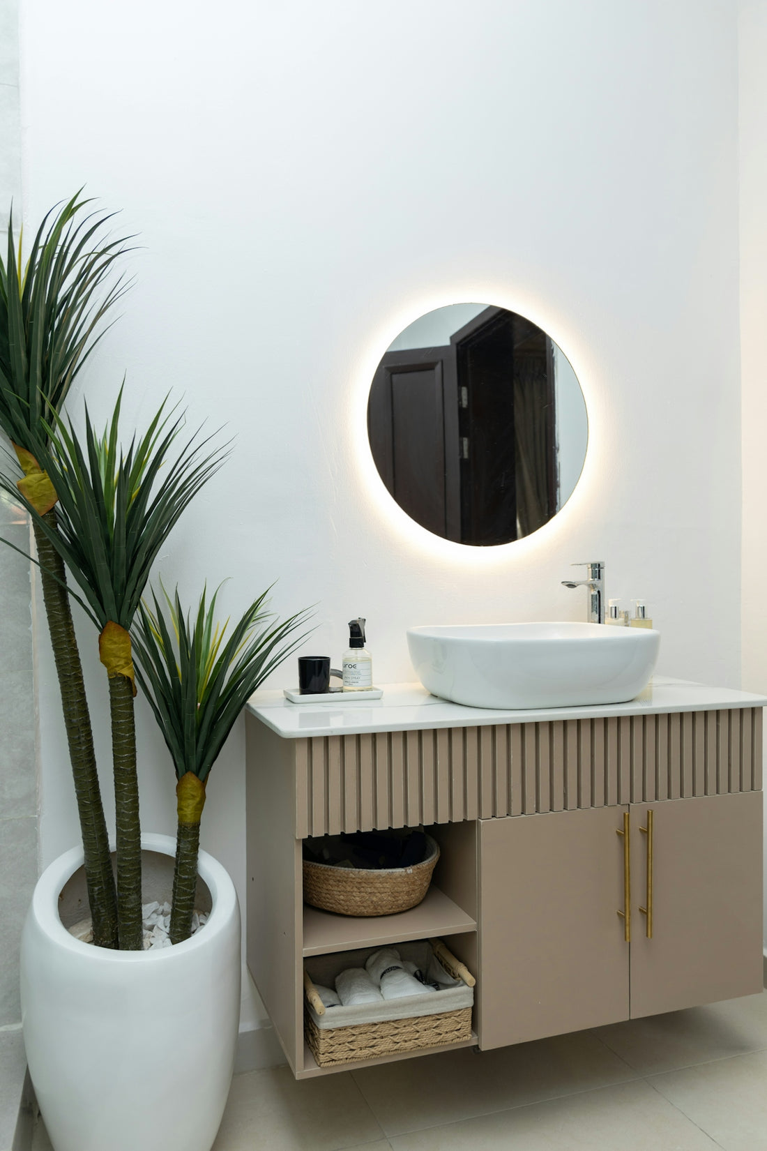 Modern bathroom vanity with illuminated mirror and potted plant.