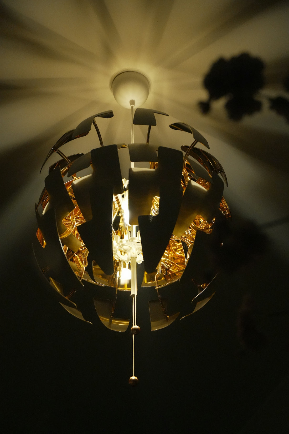 A spherical pendant light with gold interior panels casting shadows on the ceiling.