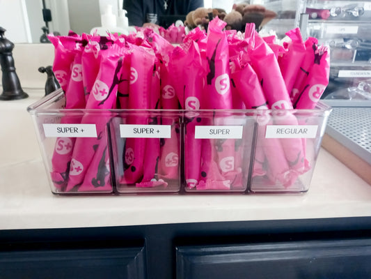 A clear plastic organizer filled with pink wrapped tampons on a bathroom counter