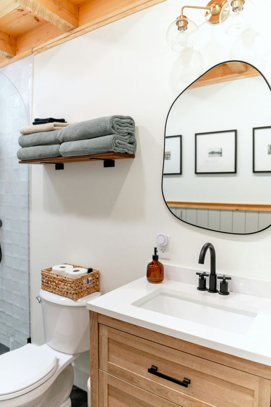 A bathroom with a wooden vanity, white sink, and an irregular mirror on a wall