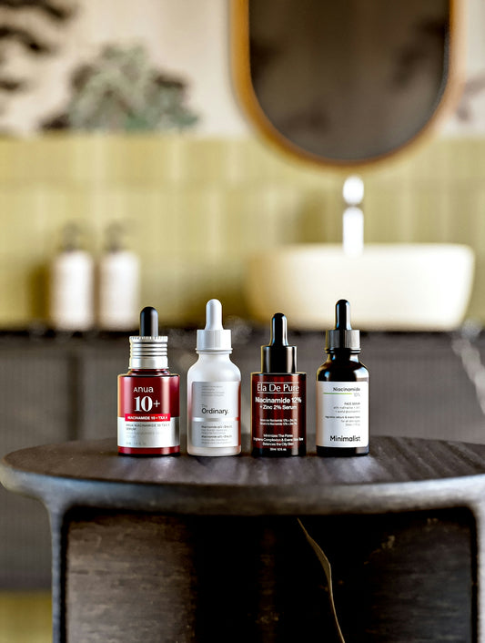 Four dropper bottles of facial serum on a dark wooden stool in a bathroom