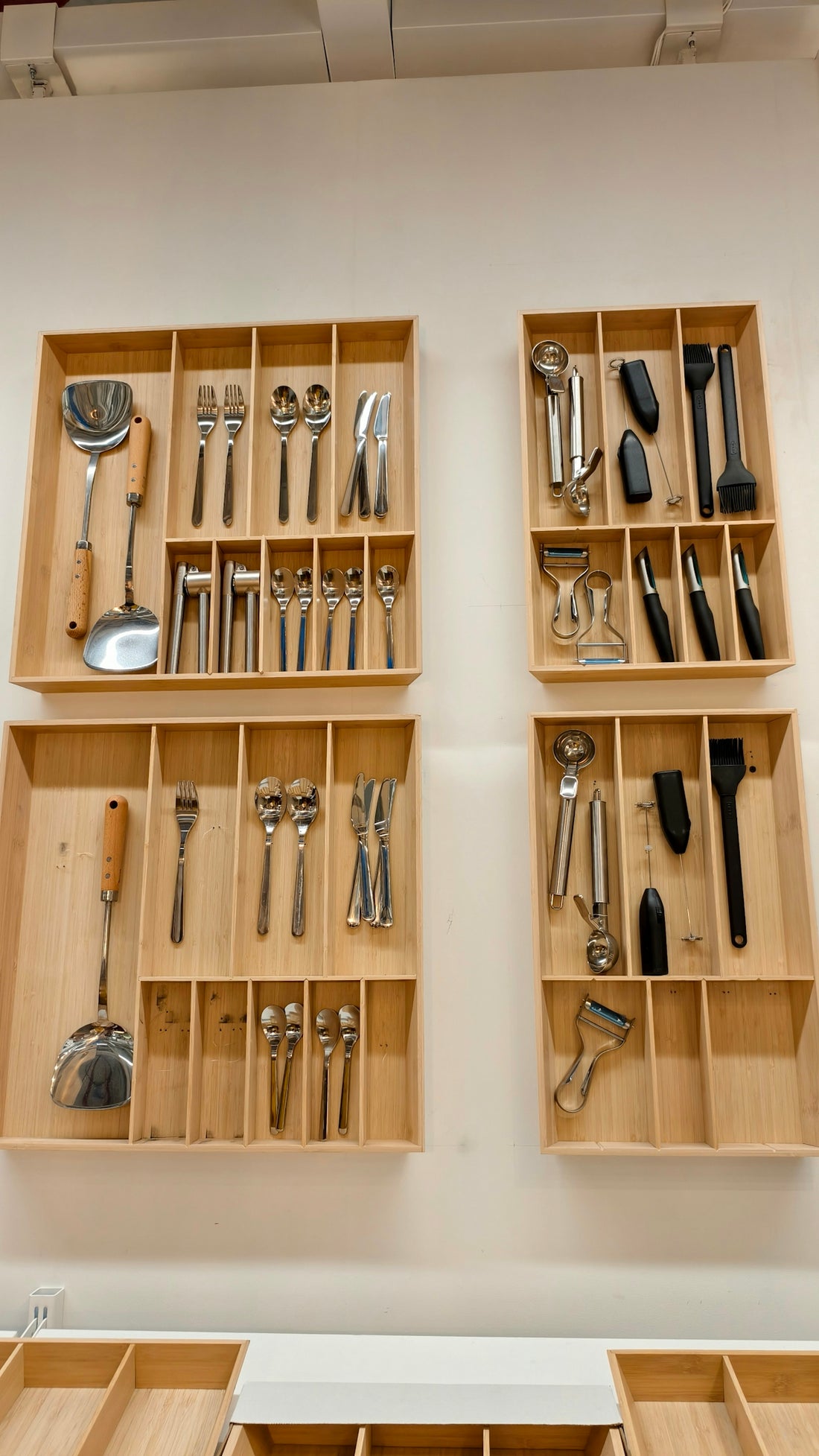 Four wooden drawer organizers mounted on a white wall containing various kitchen utensils