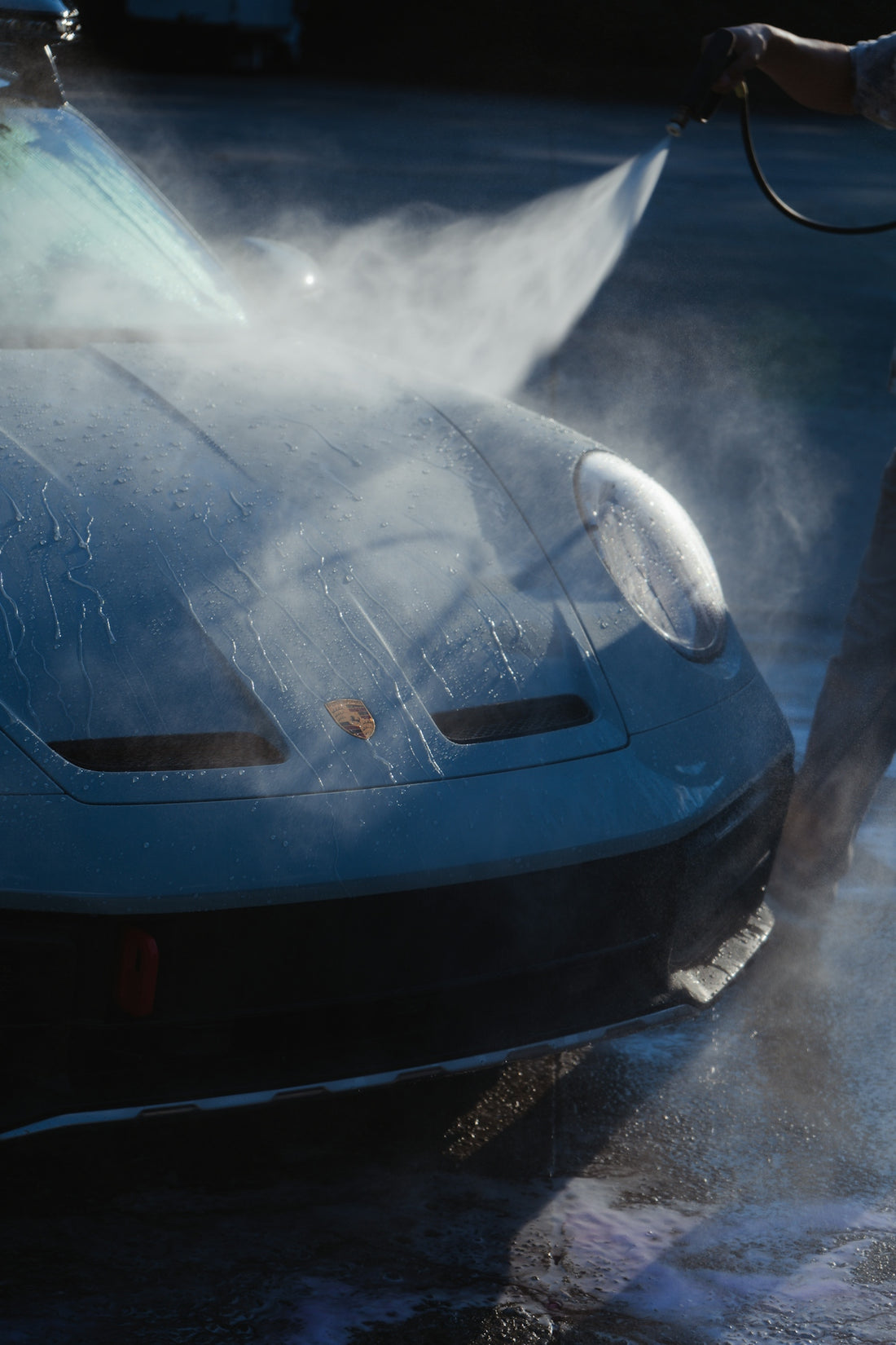 A person spraying water from a hose onto a light blue sports car