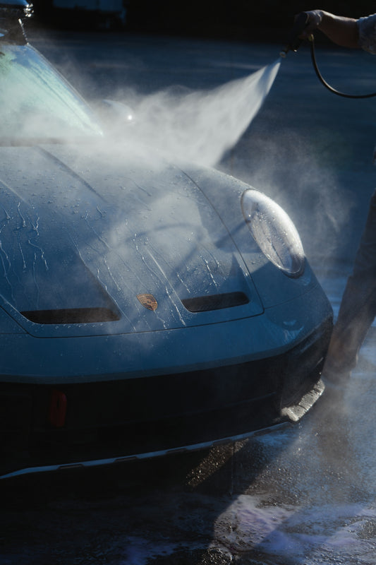 A person spraying water from a hose onto a light blue sports car