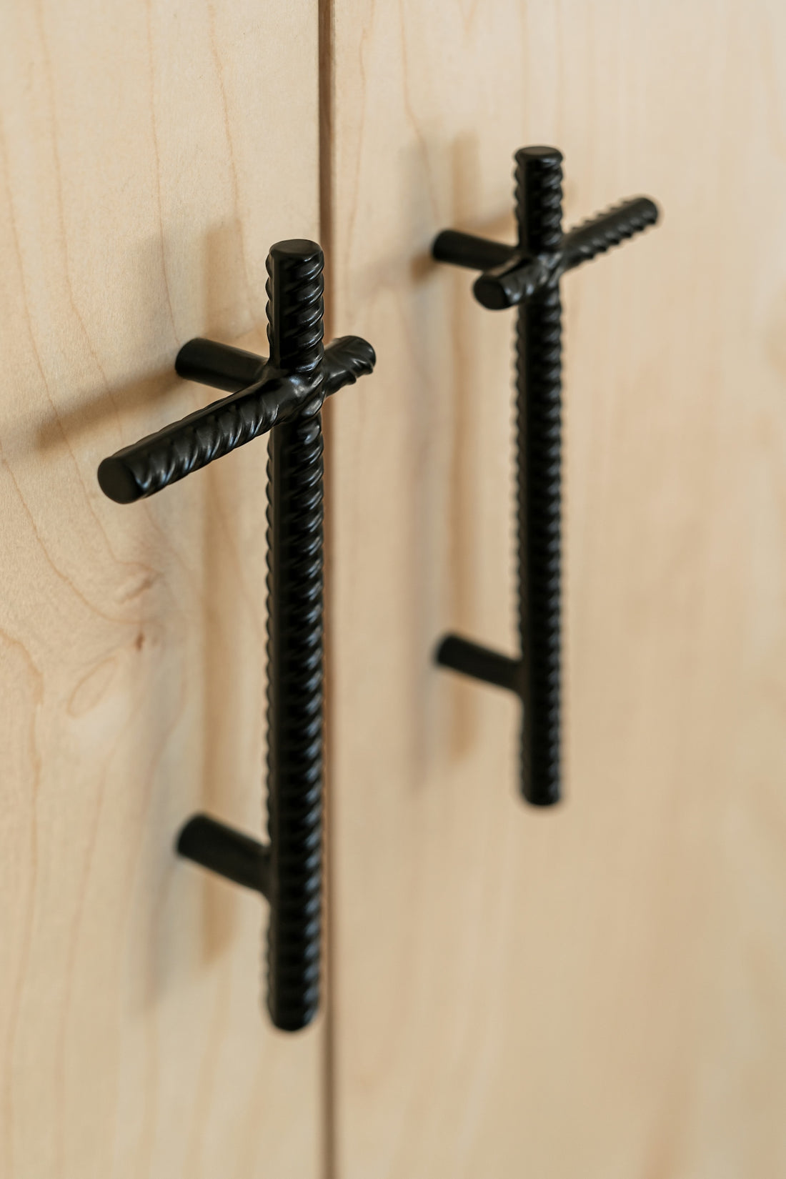 Two black rebar cabinet handles mounted on light wood doors